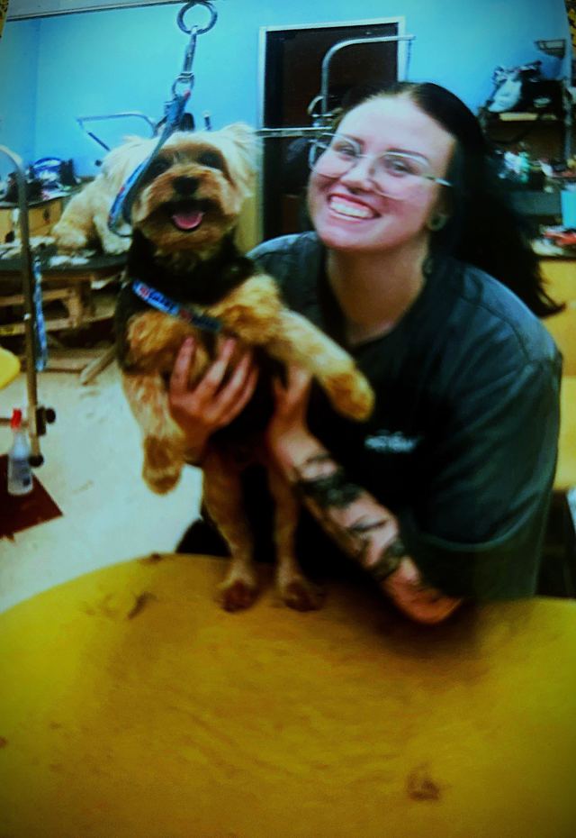 Tatyana smiling with a freshly groomed Yorkie on the grooming table